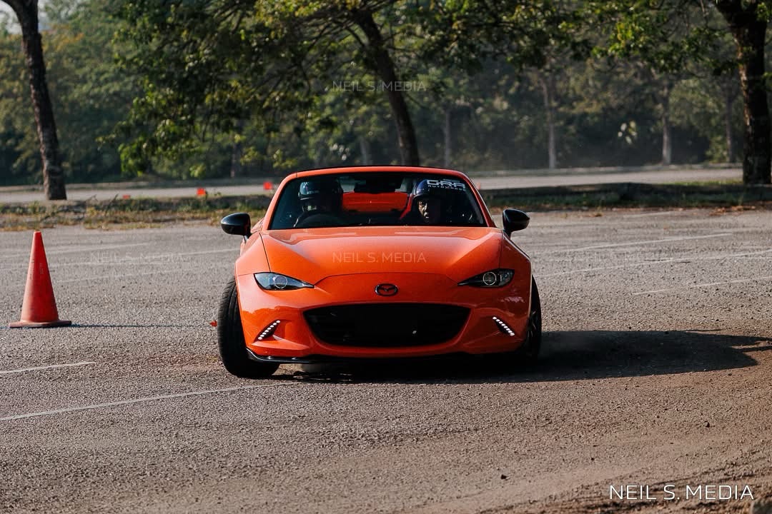 Racing orange Mazda MX-5 RF attacking a gymkhana course at speed